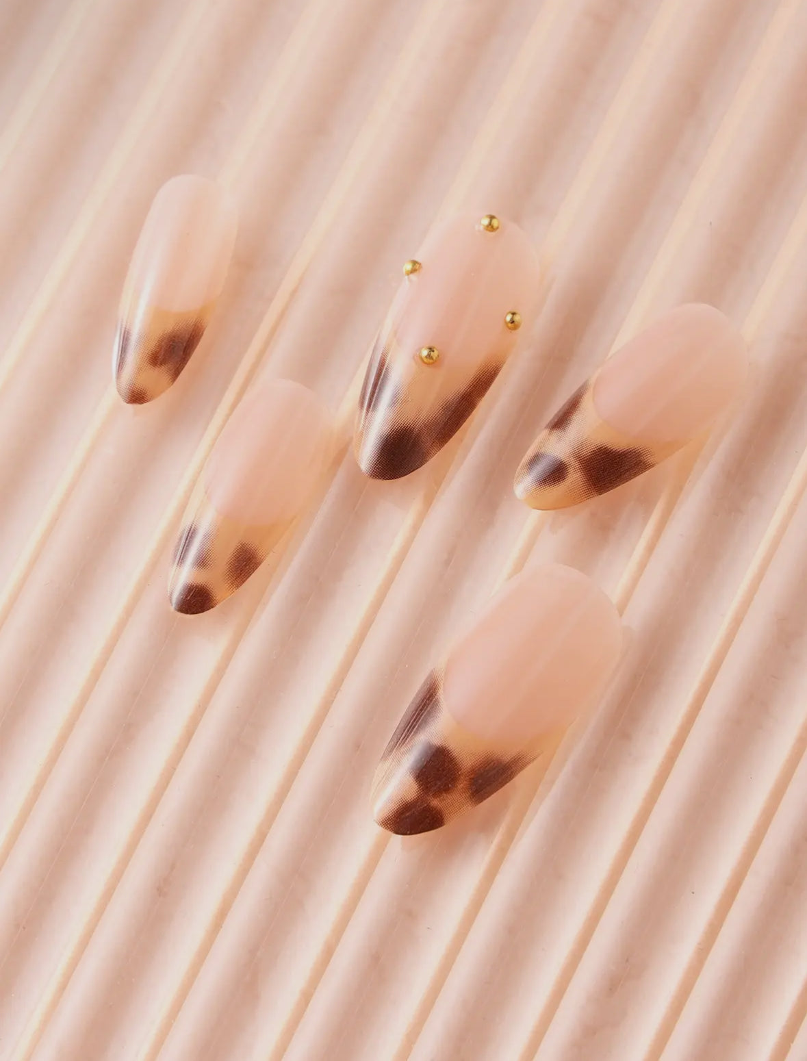 Nails with tortoiseshell design and gold accents on a neutral background