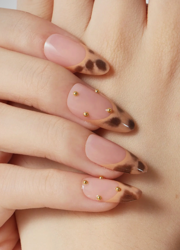 Close-up of a hand with tortoiseshell nail design and gold accents on a neutral background
