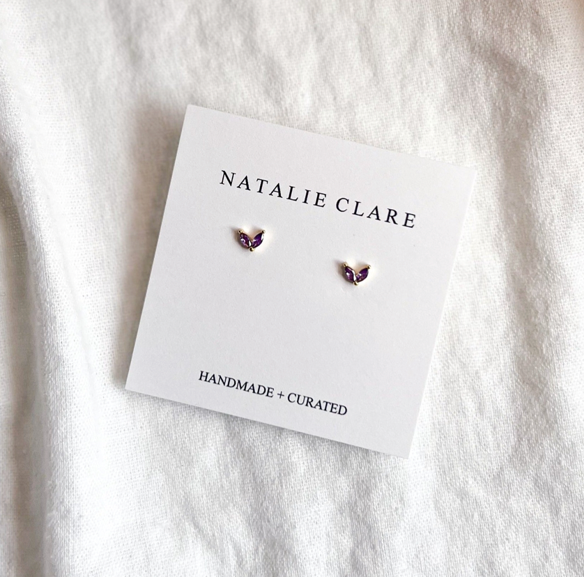 Butterfly-shaped earrings on a 'Natalie Clare' branded card against a white fabric background