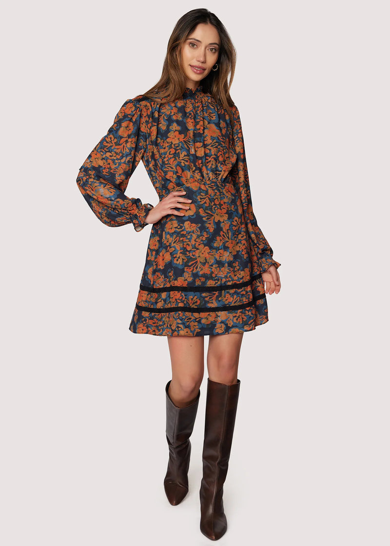 Woman wearing a floral dress with long sleeves and brown boots on a white background