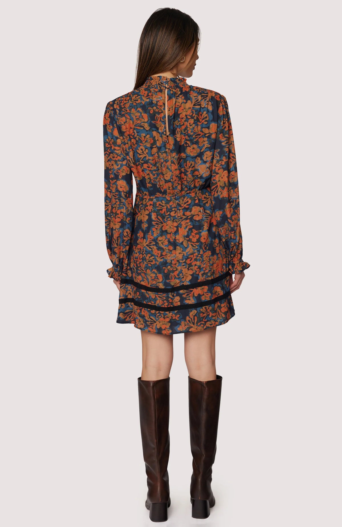 Woman wearing a floral dress with long sleeves and brown knee-high boots on a white background