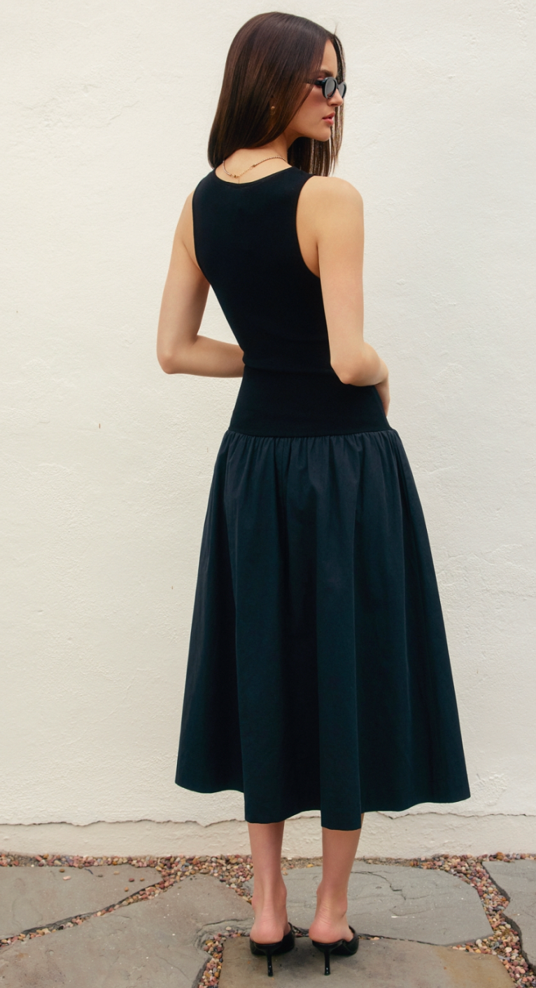 Woman wearing a black sleeveless dress against a white wall.