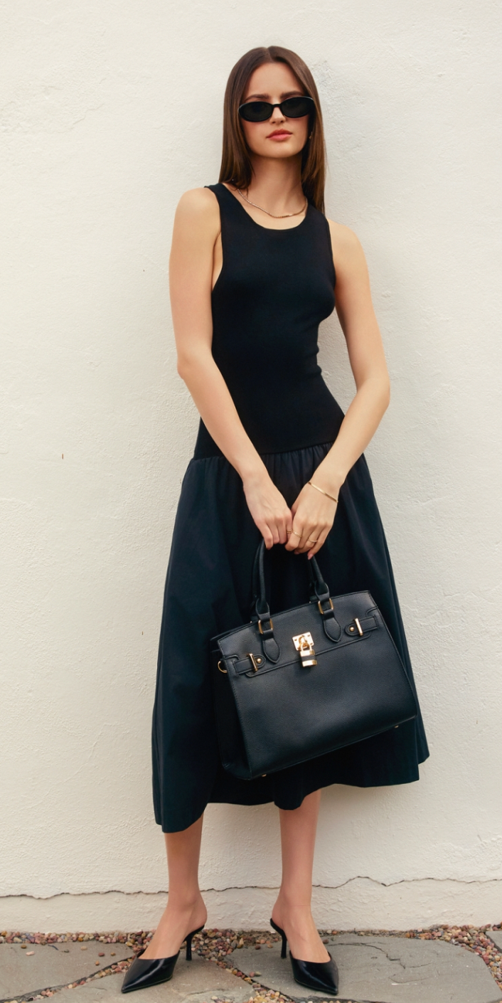 Woman in a black dress holding a black handbag against a white wall