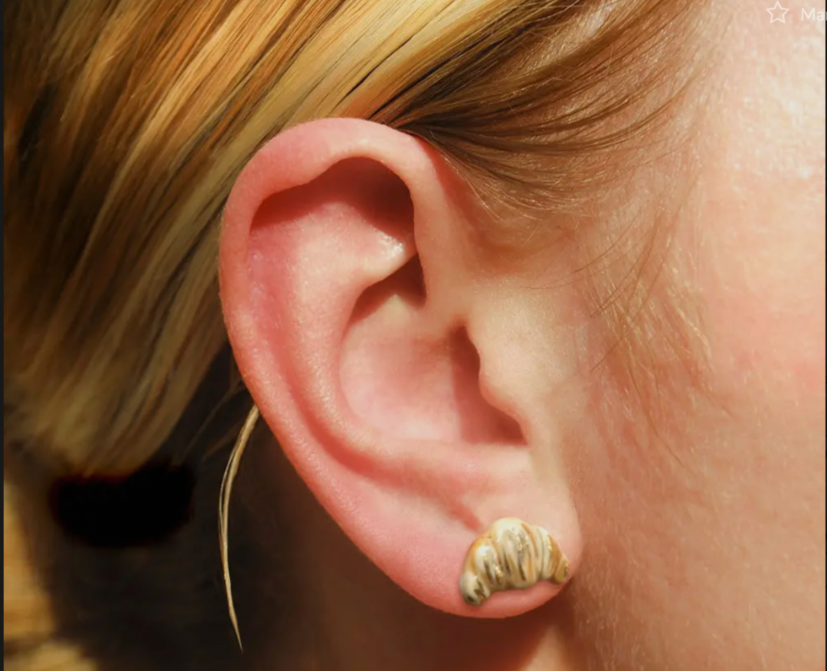 Close-up of an ear wearing a gold earring with a blurred background