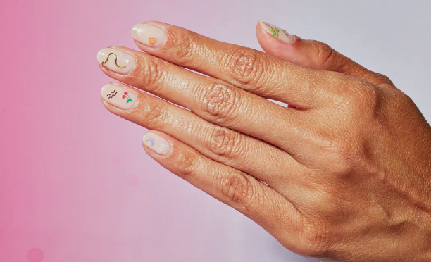 Hand with decorated nails against a pink background