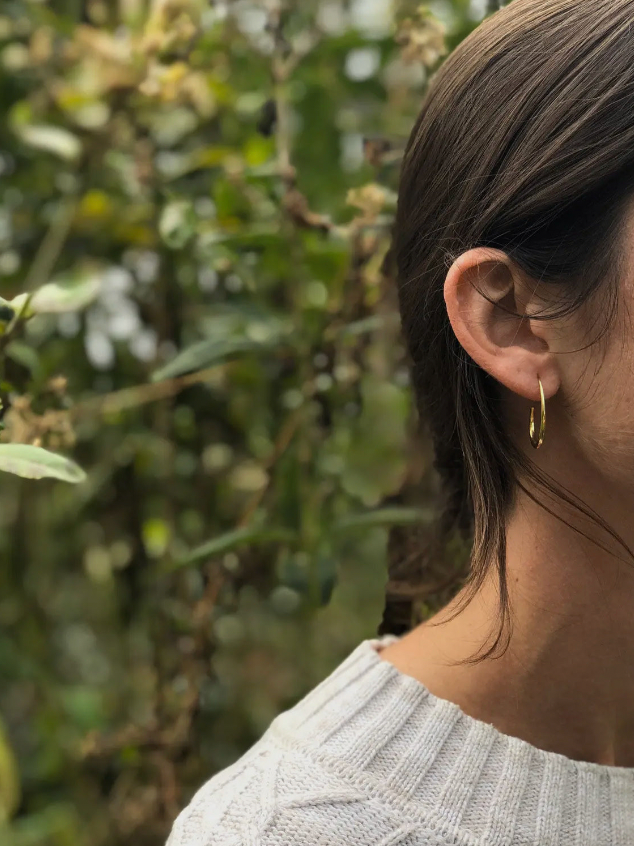 Person wearing a gold earring with a blurred green background