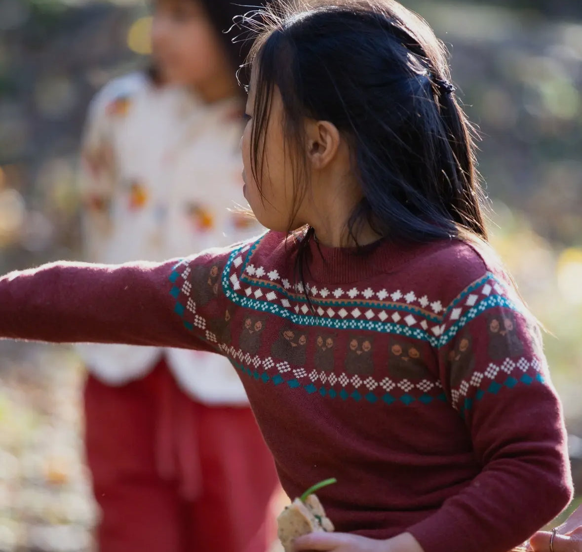 Child wearing a patterned sweater with another child in the background