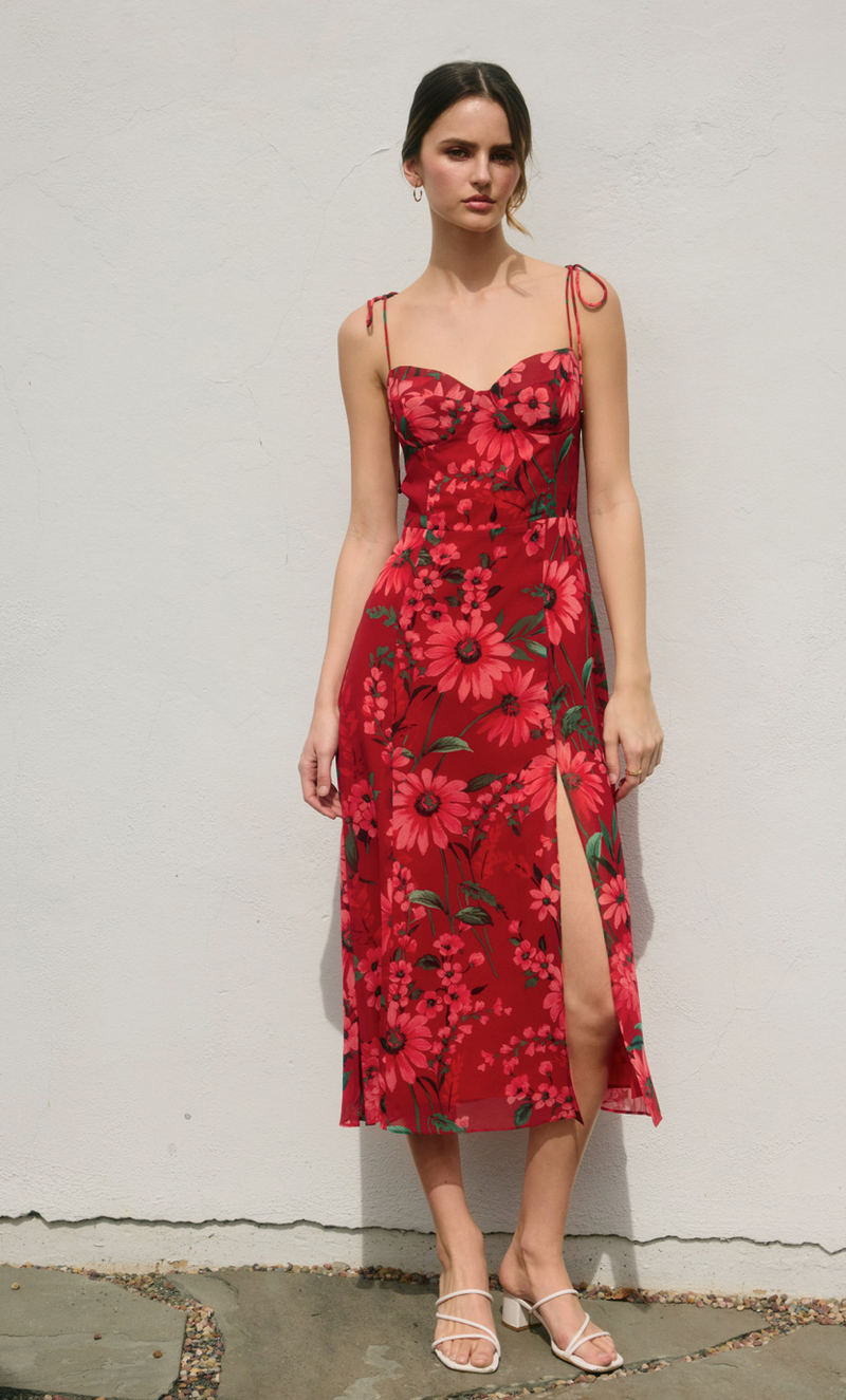 Woman wearing a red floral dress against a white wall.