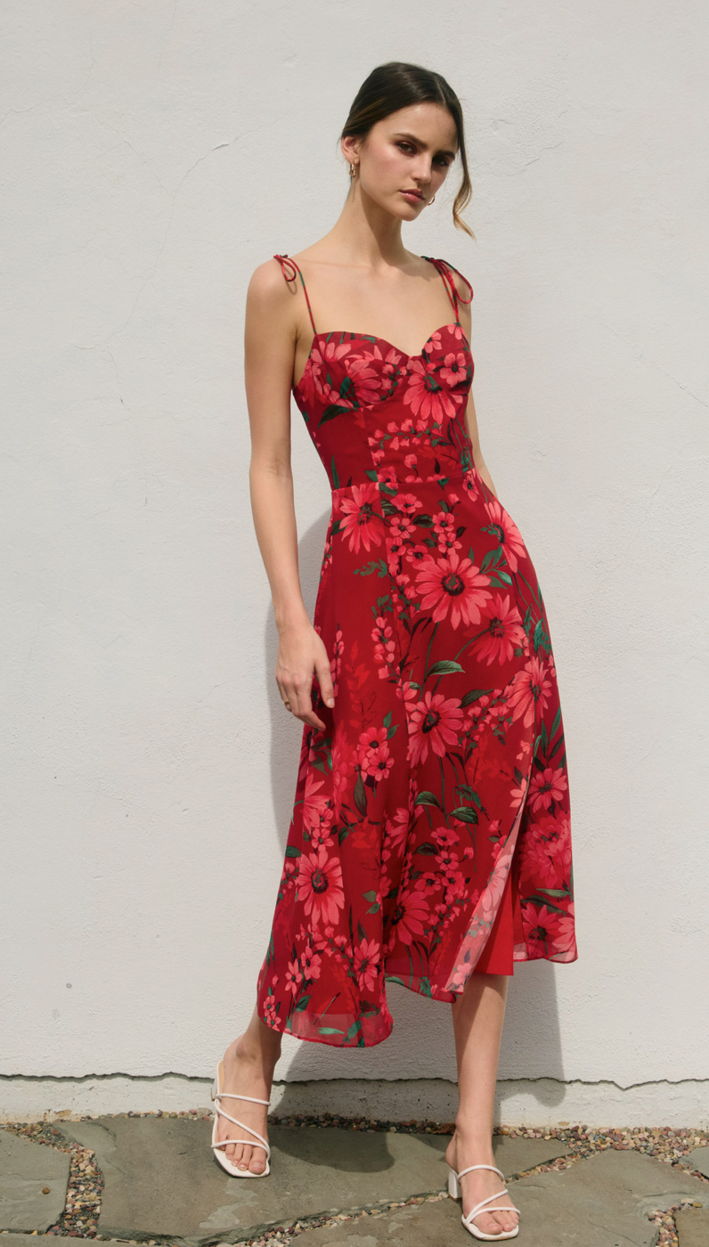 Woman wearing a red floral dress against a white wall.