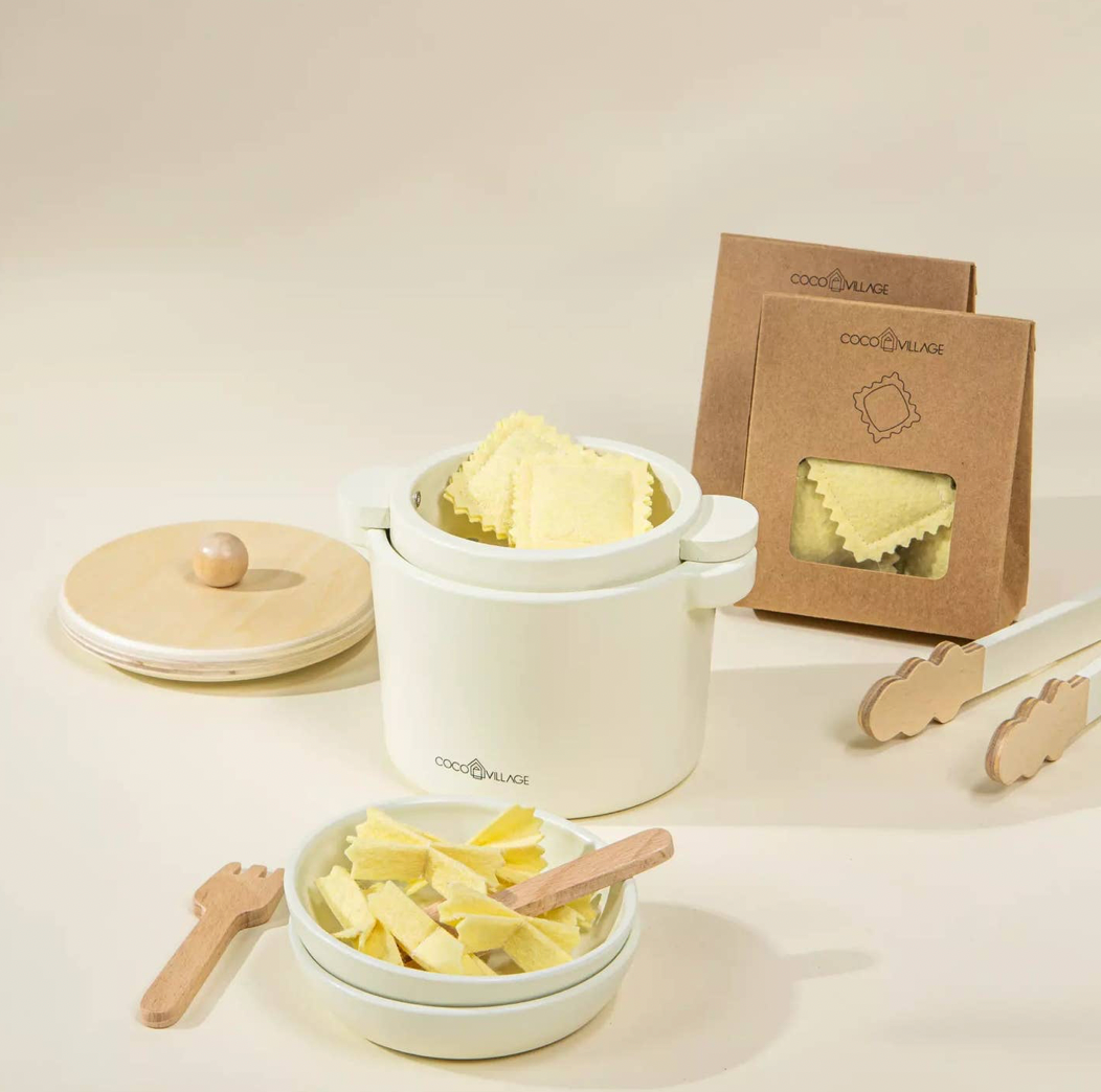 White ceramic container with pasta, wooden tools, and a brown package on a light background