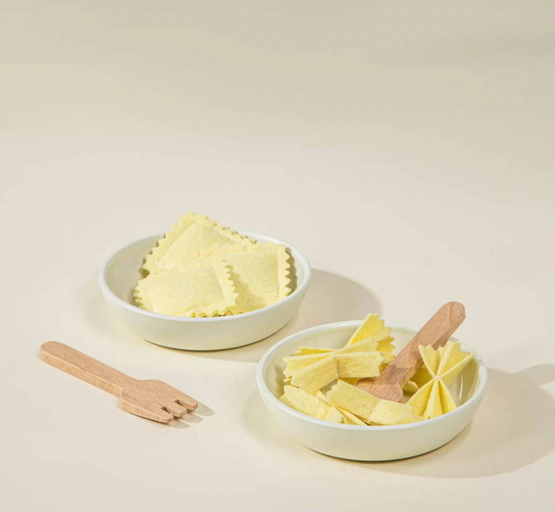Two bowls of ravioli with wooden tools on a light background