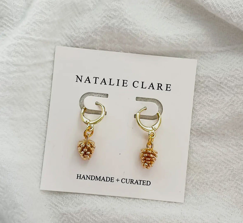 Gold pine cone earrings on a 'Natalie Clare' branded card with a light gray background. 