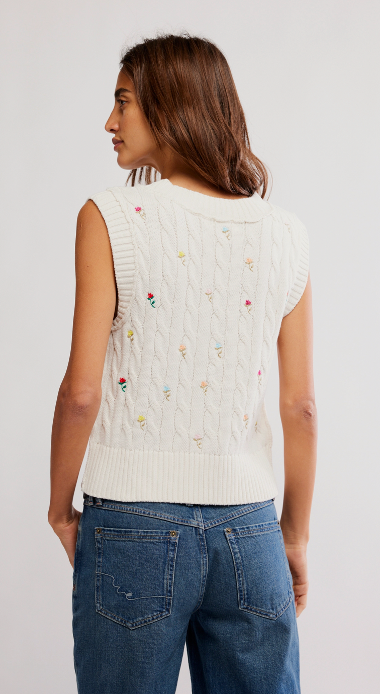 Woman wearing a sleeveless knitted top with colorful patterns and blue jeans on a white background