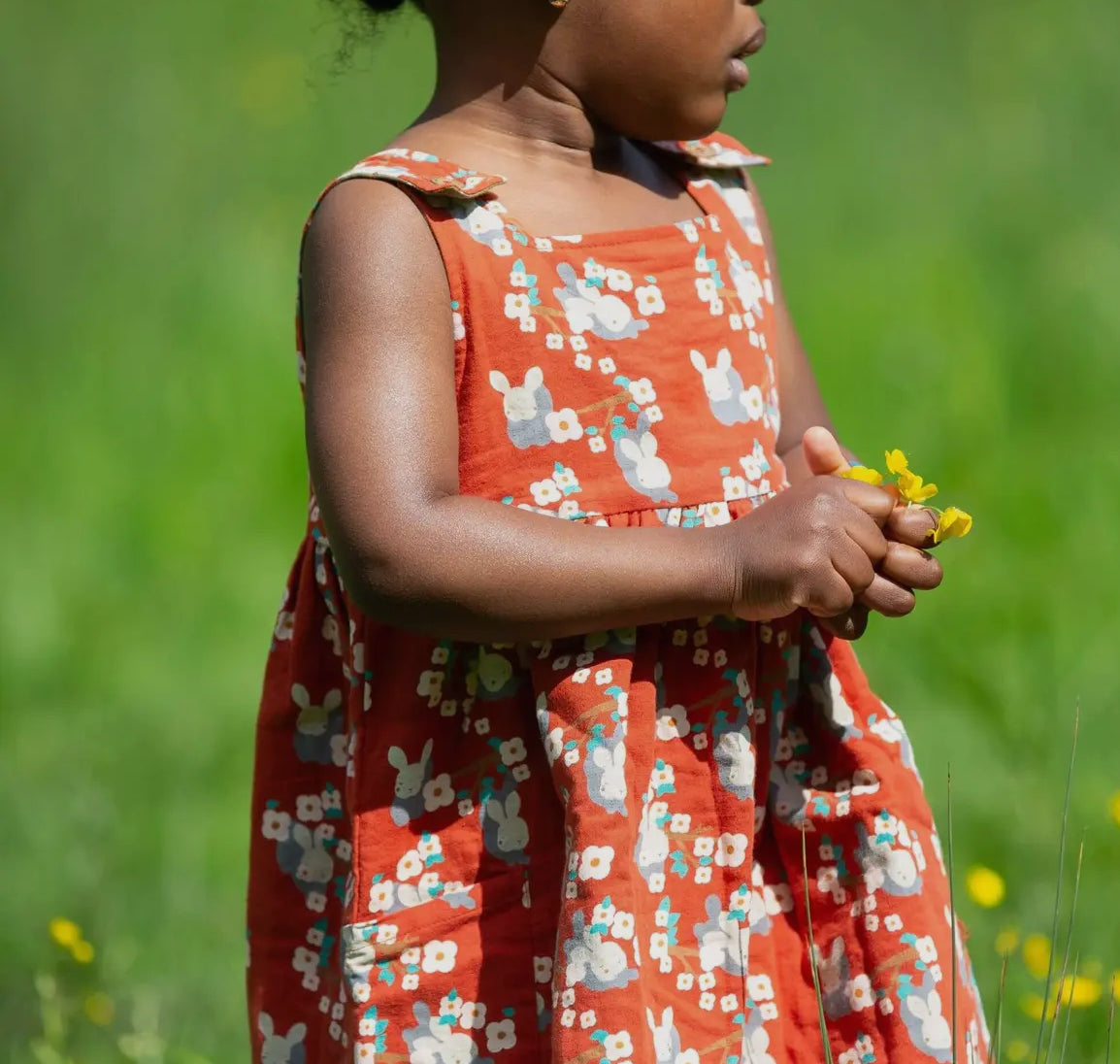 Young girl in a red floral dress holding flowers in a grassy field
