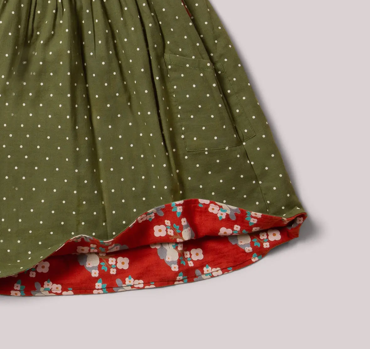 Close-up of a green dress with white polka dots and a red floral hem on a light gray background