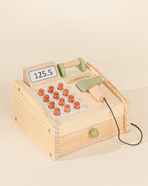 Wooden toy cash register with coins on a beige background
