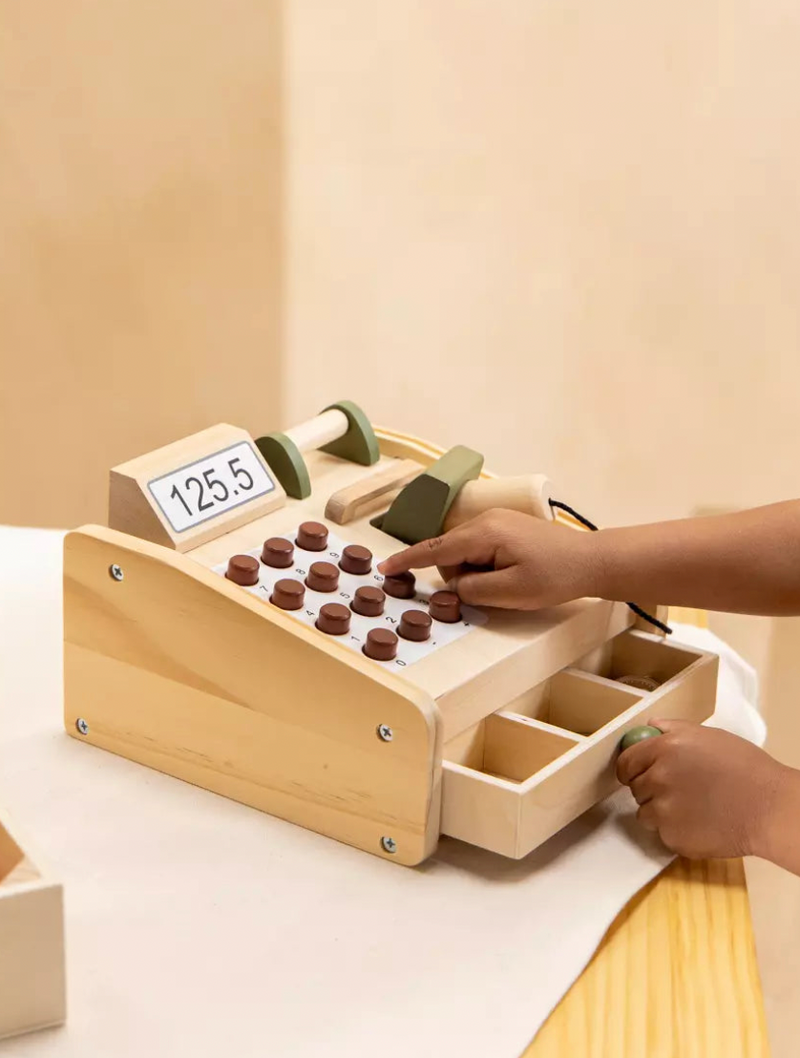 Wooden cash register toy with hands interacting on a light background