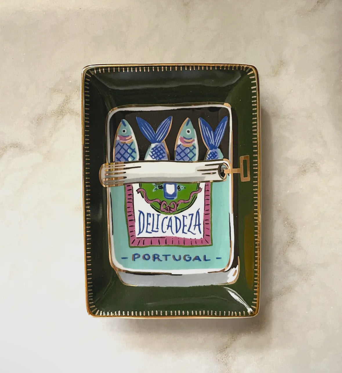 Decorative tray with fish design and 'Delicadeza Portugal' branding on a marble surface