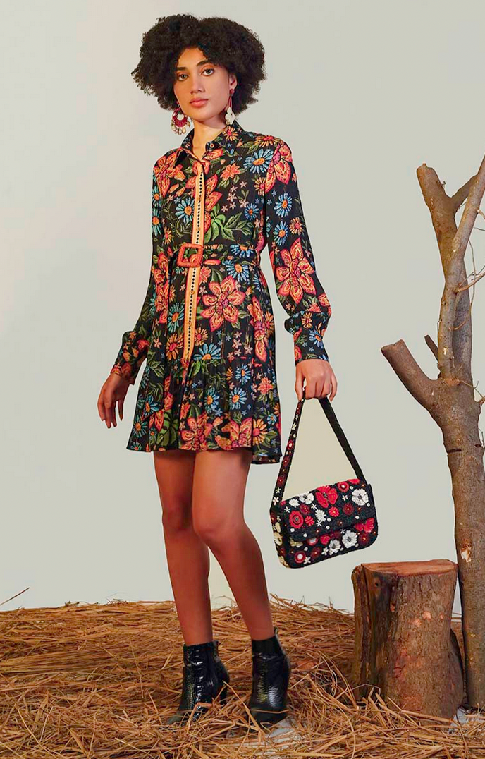 Woman in a floral dress holding a matching handbag next to a tree stump.