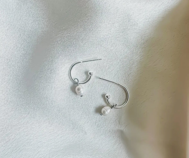 Silver earrings with pearls on a light fabric background