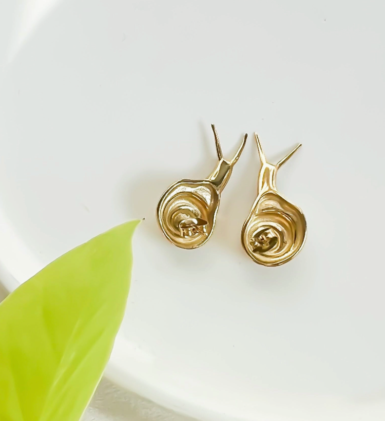 Gold snail-shaped earrings on a white background with a green leaf.