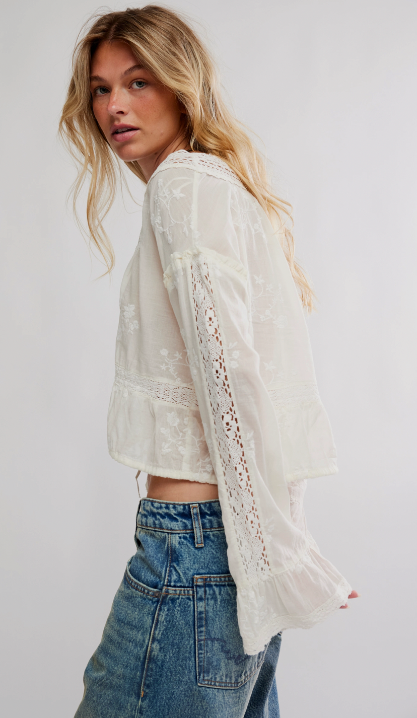 Woman wearing a white lace top and blue jeans on a plain background