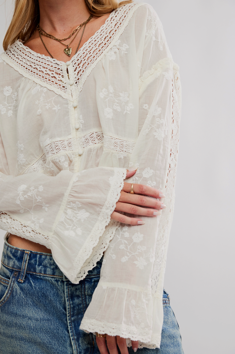 White lace blouse worn over blue jeans on a plain background
