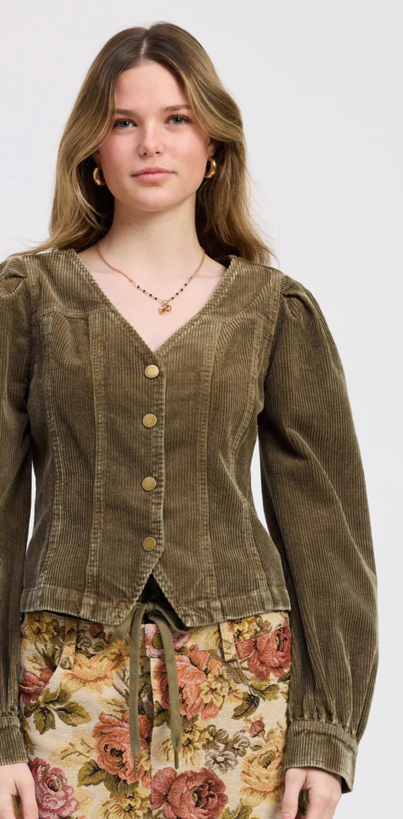 Woman wearing a corduroy jacket over a floral dress on a white background
