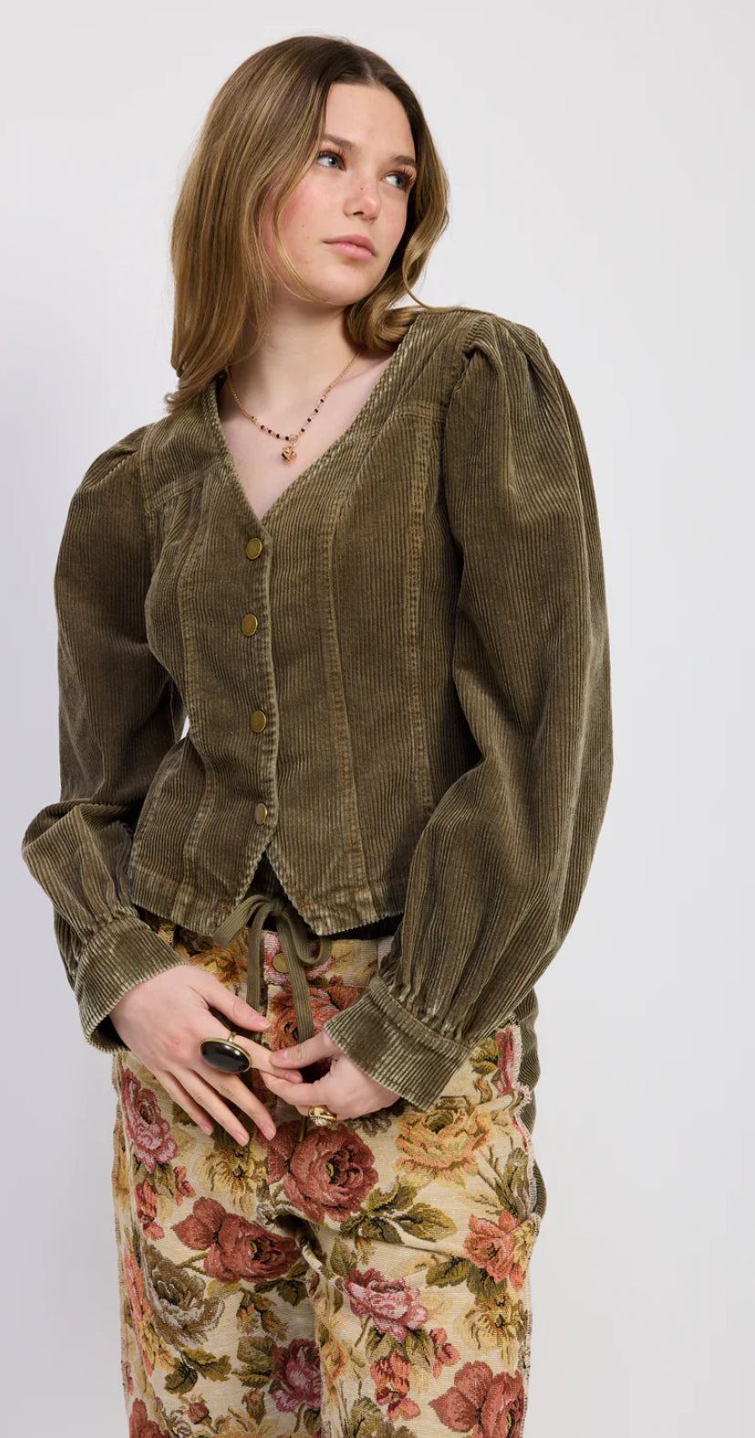 Woman wearing a vintage-style green jacket and floral skirt on a white background