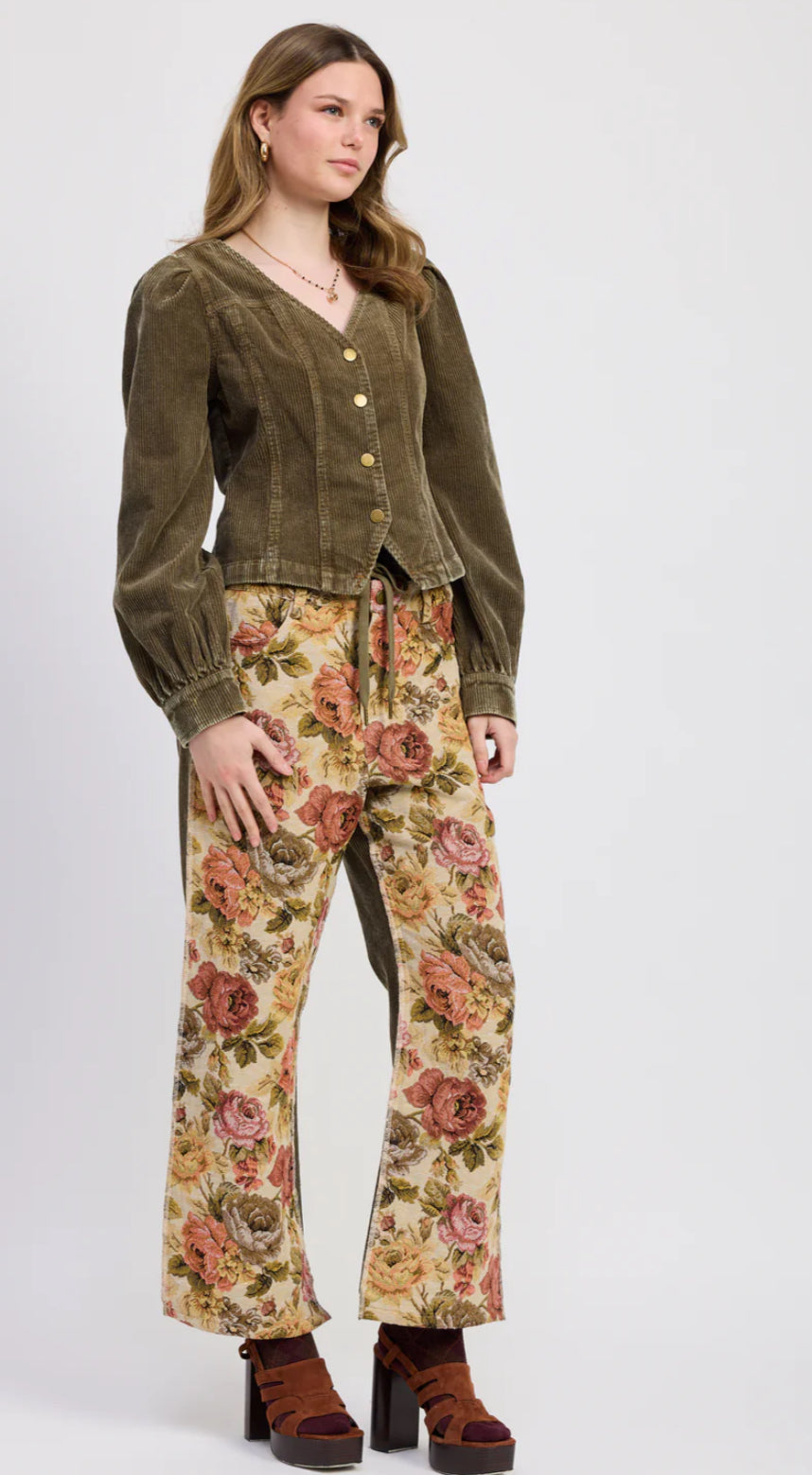 Woman wearing a brown corduroy jacket and floral pants on a white background
