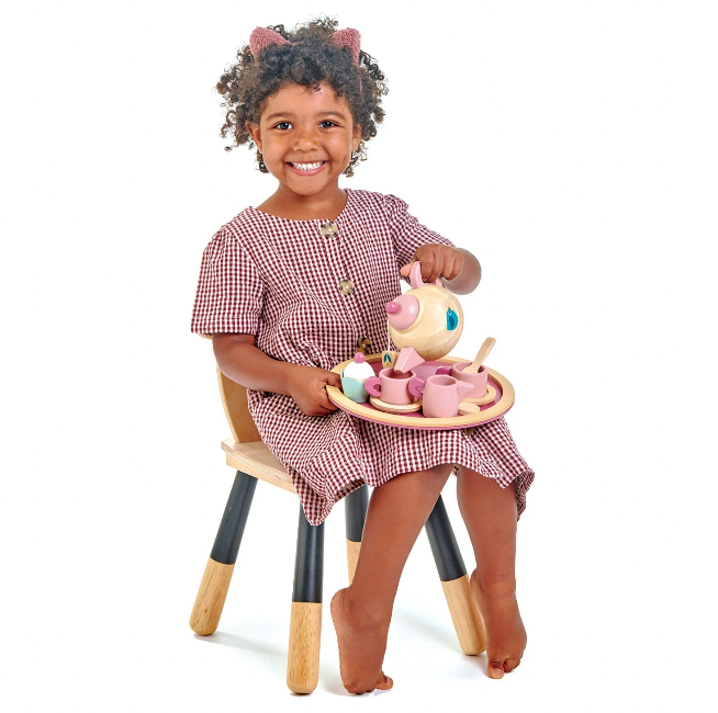 Child in a checkered dress playing with a toy tea set on a white background