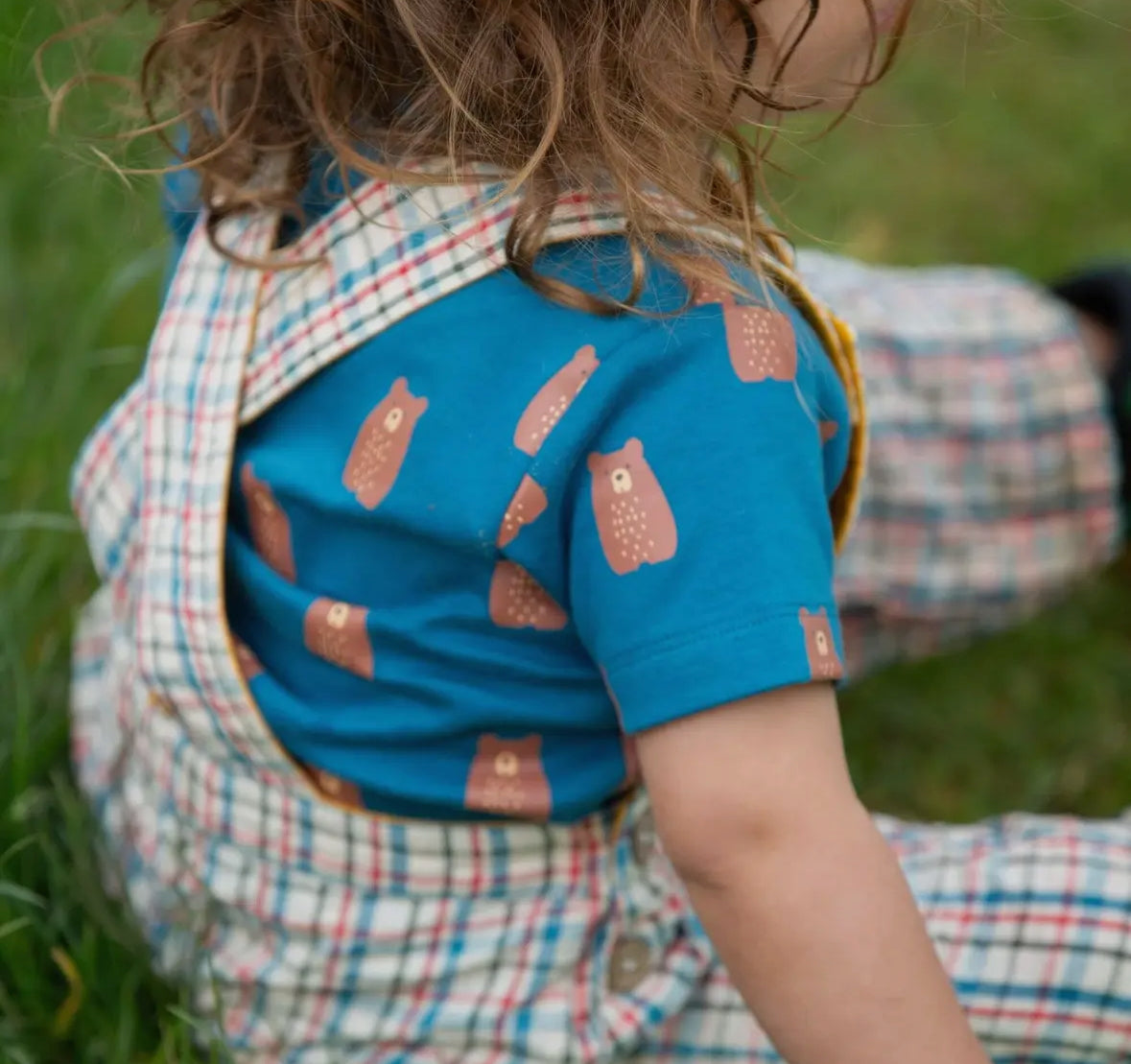 Child wearing a blue shirt with bear prints and a plaid vest outdoors.