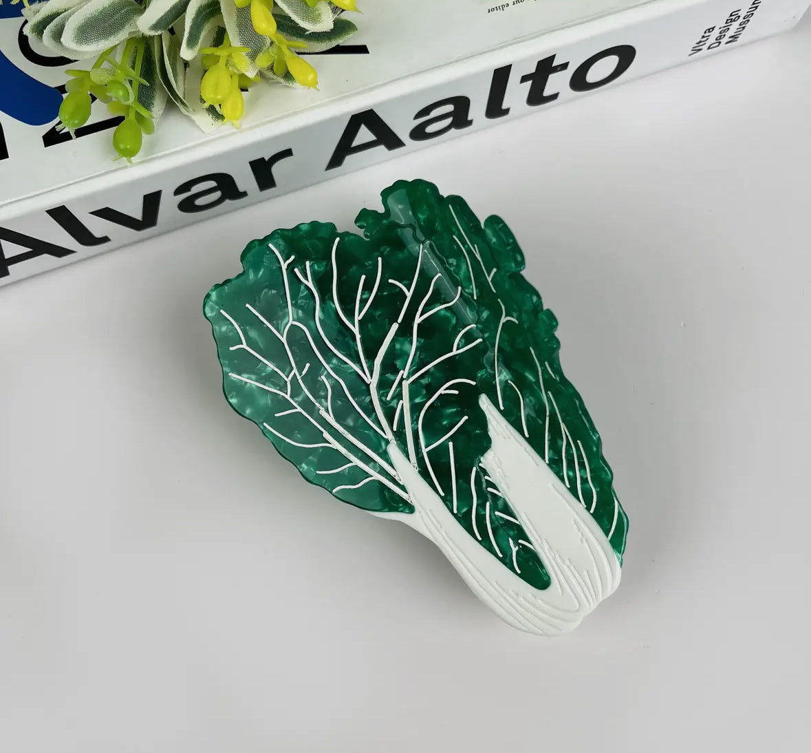 Green leaf-shaped object on a white surface with 'Alvar Aalto' branding in the background.