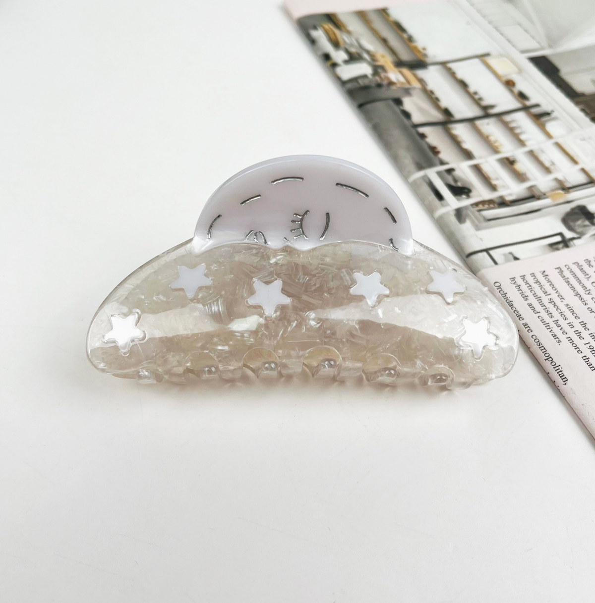 Clear cloud-shaped object with star patterns on a white surface with a magazine in the background