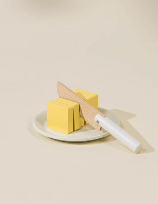 Two yellow cubes on a white plate with a knife on a beige background