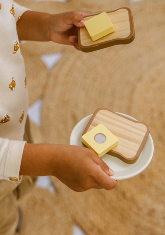 Wooden toy bread with butter held by a child on a wooden surface