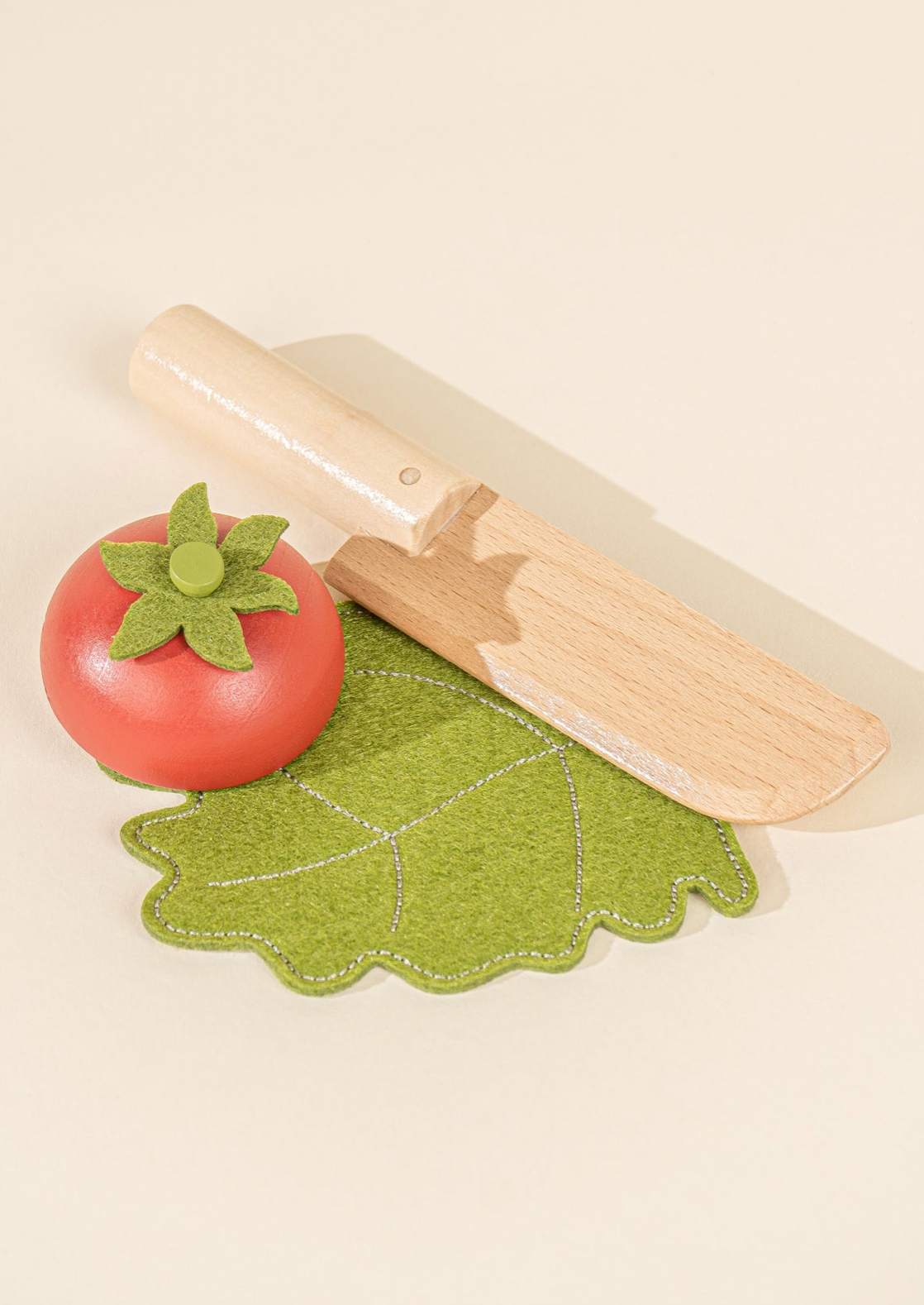 Wooden rolling pin with a red tomato and green leaf on a beige background