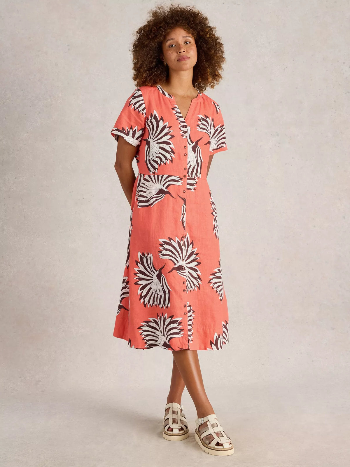 Woman wearing a coral dress with black and white pattern against a neutral background