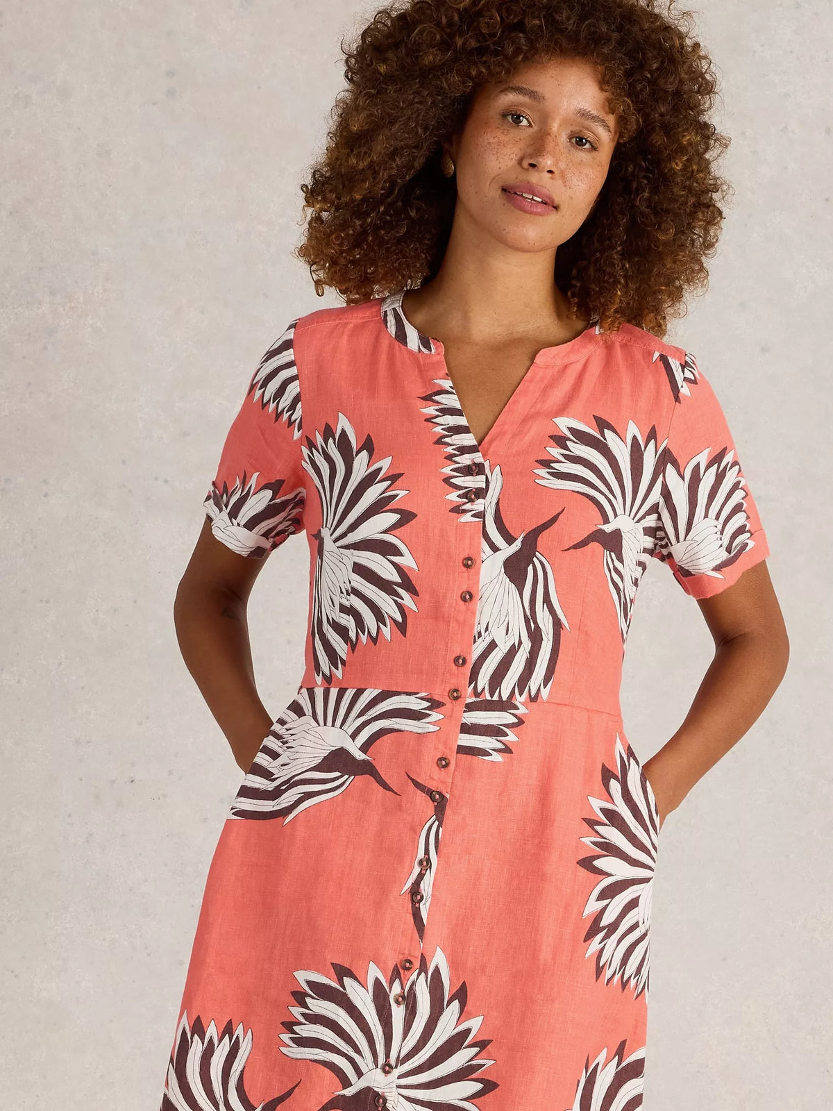 Woman wearing a coral dress with black and white floral pattern against a neutral background