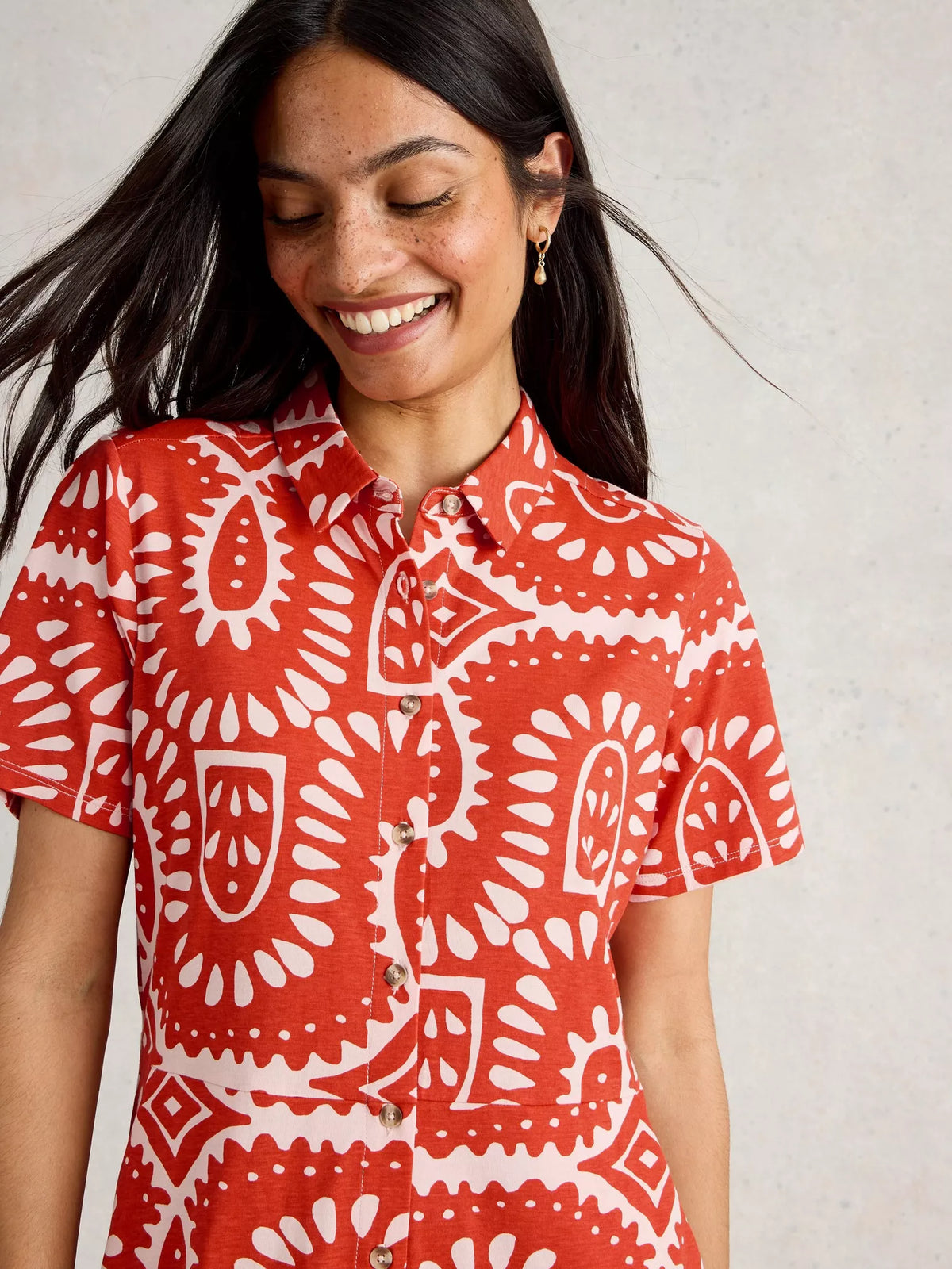 Woman wearing a red and white patterned shirt against a neutral background
