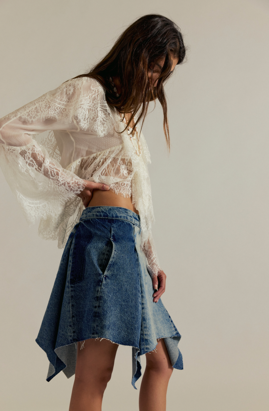 Woman wearing a white lace top and denim skirt against a plain background