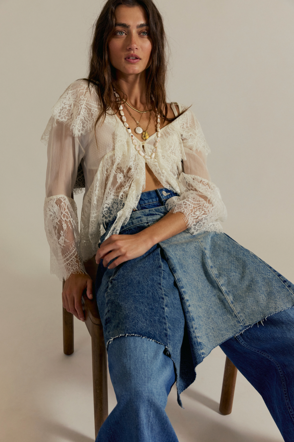 Woman wearing a sheer white top and blue jeans sitting on a chair.
