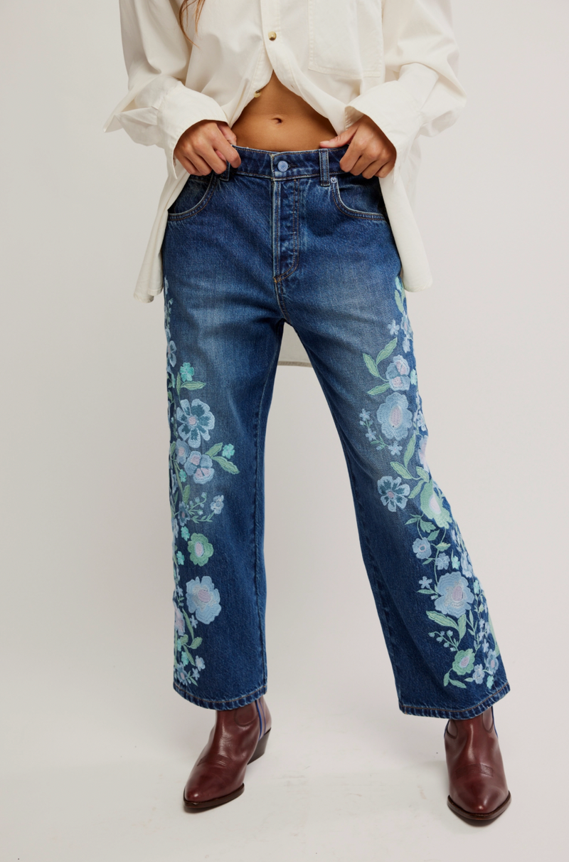 Person wearing blue jeans with floral patterns on a white background