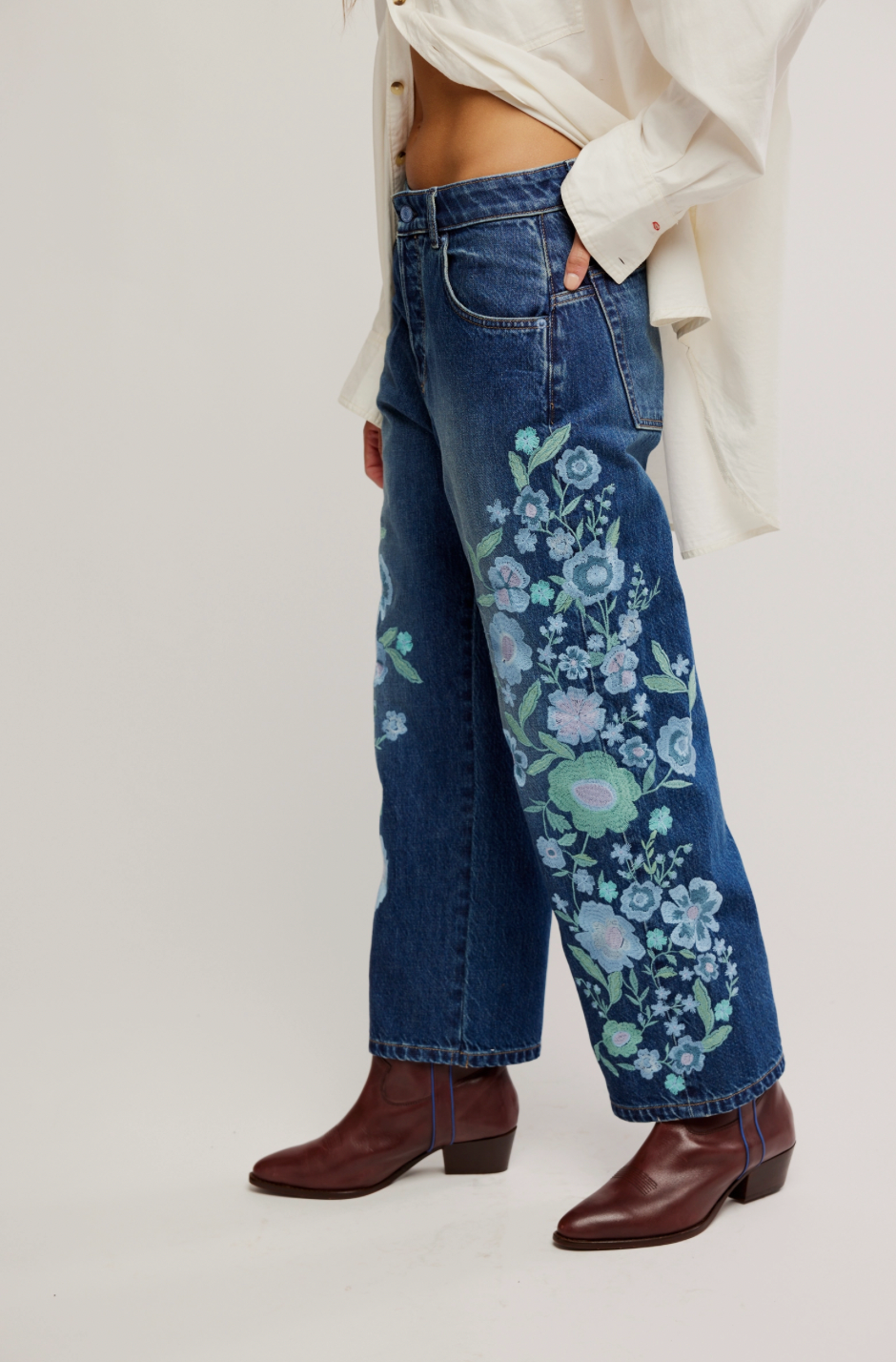 Blue jeans with floral embroidery worn by a person on a white background