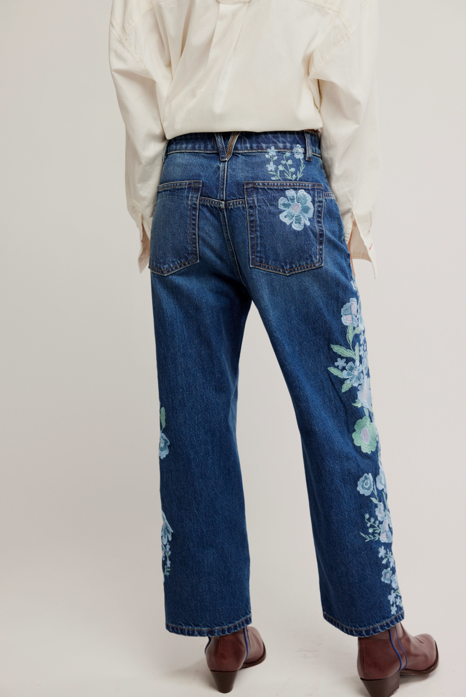 Blue jeans with floral embroidery worn by a person on a plain background