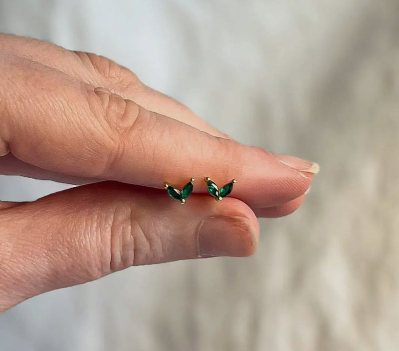 Hand holding a pair of green earrings against a neutral background