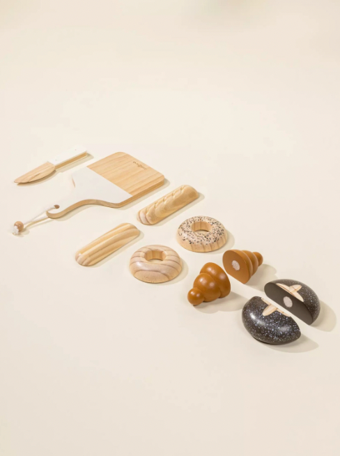 Set of toy bakery items including bread, donuts, and a cutting board on a beige background