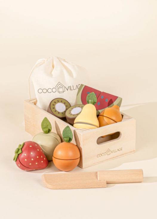 Set of wooden toy fruits and vegetables in a crate with a coco village  branded bag on a beige background.