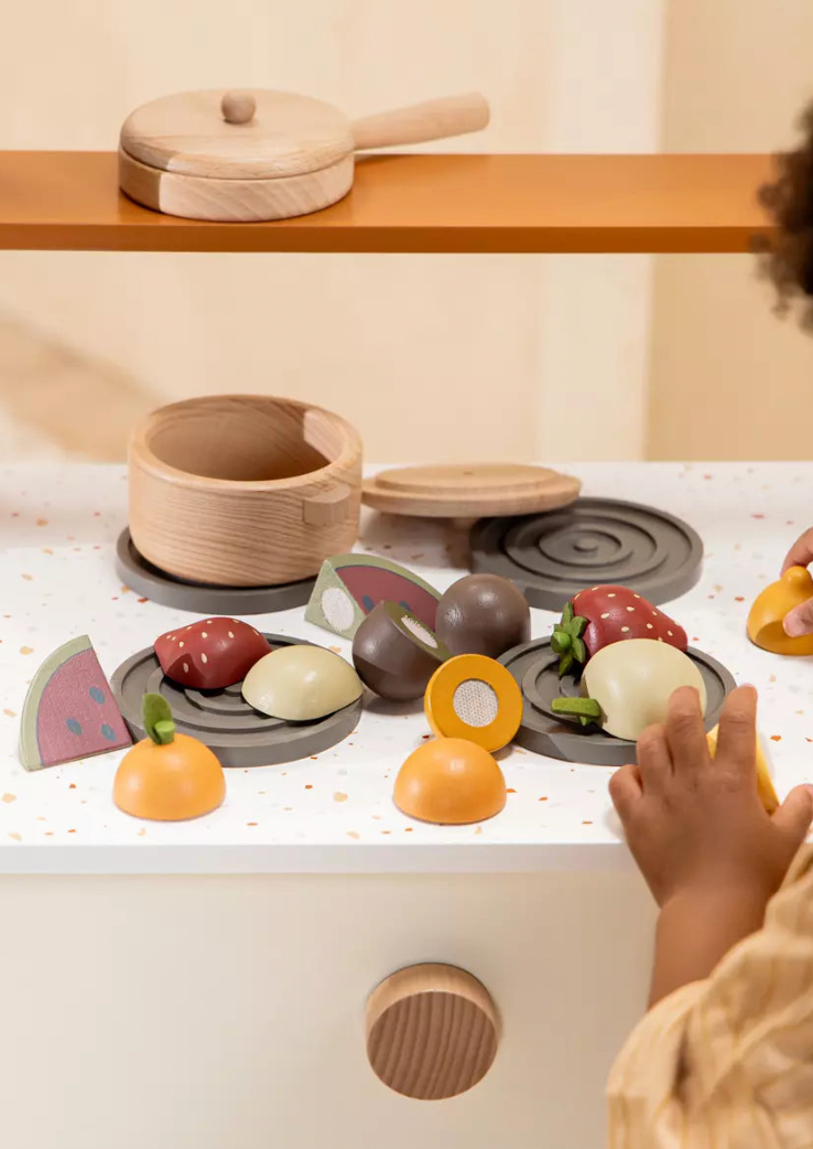 Child playing with a wooden toy kitchen set on a white surface.