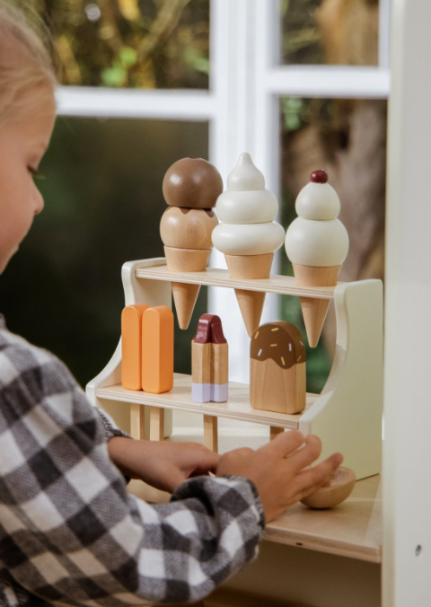 Child playing with wooden ice cream cones and toys on a shelf.